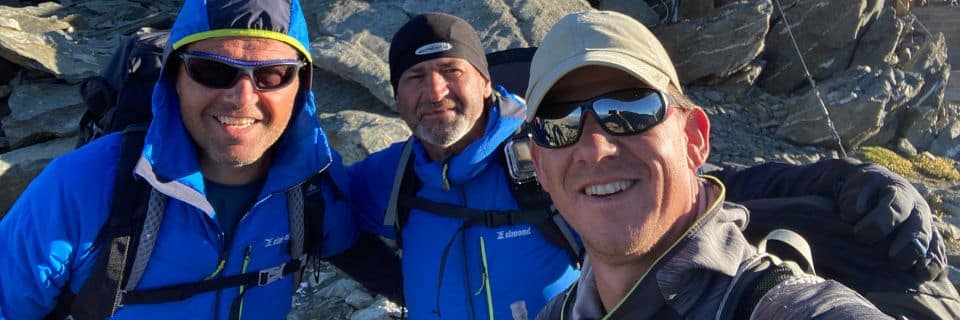 v.l.n.r. Steven Boets en Guy Bleyen van Partner Safety met Karl Van der Auwera van Consultrix. Ze staan op een bergtop, met rotsen achter hen. We zien alleen hun gezichten.